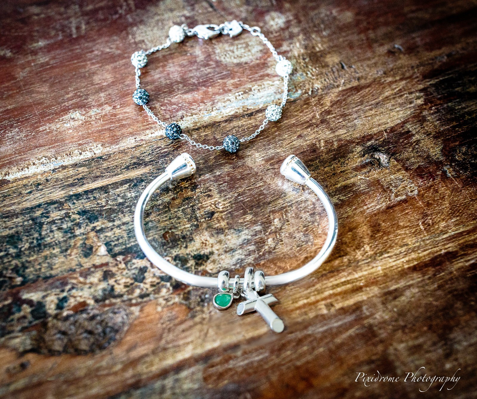 A silver charm bracelet and bangle laid on weathered wood