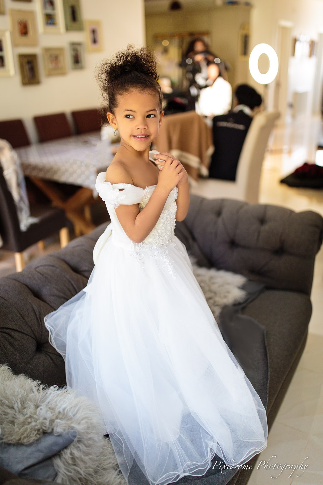 A flower girl in a white dress standing on a sofa during preparations