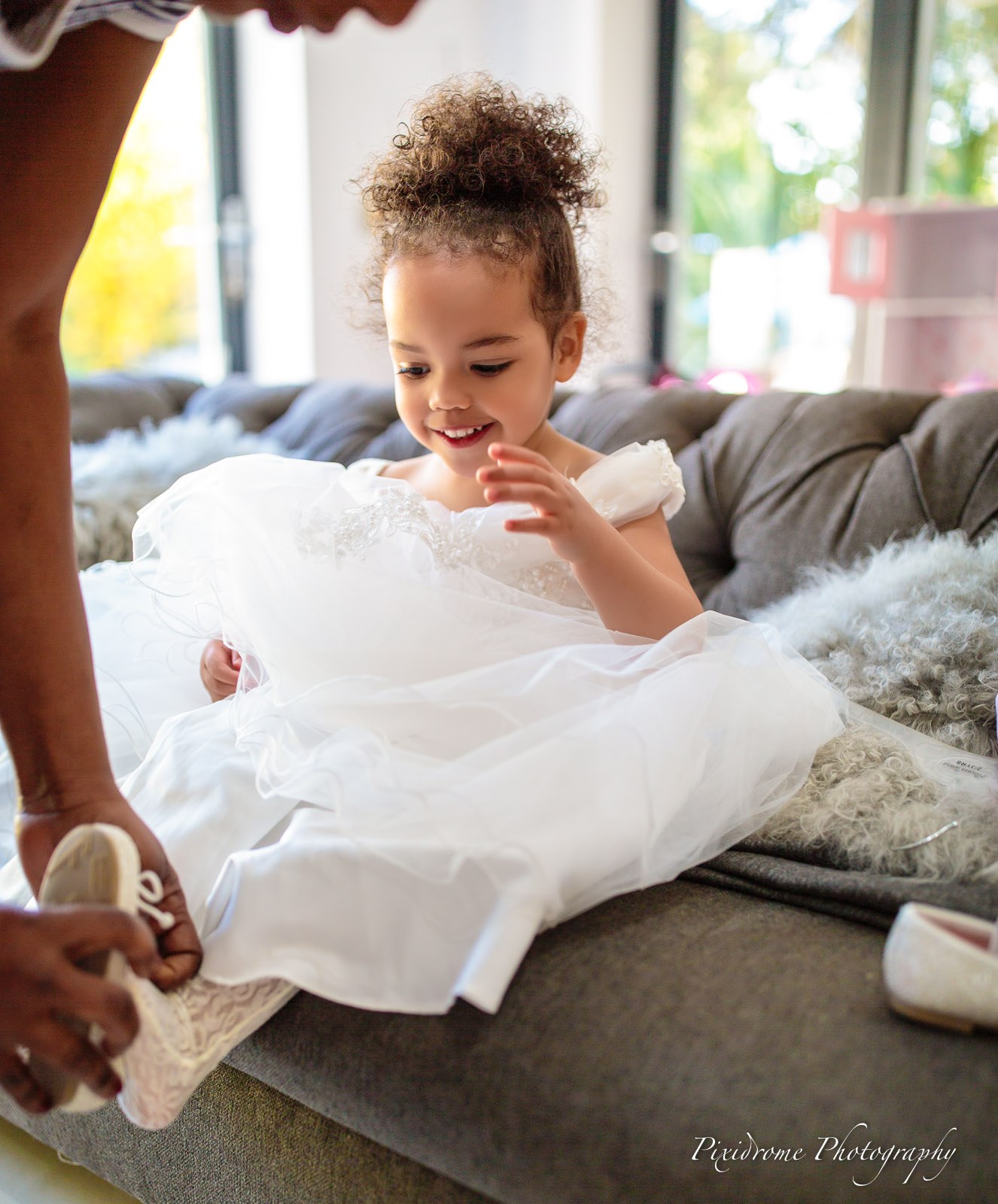 A flower girl having her shoes fastened on the sofa