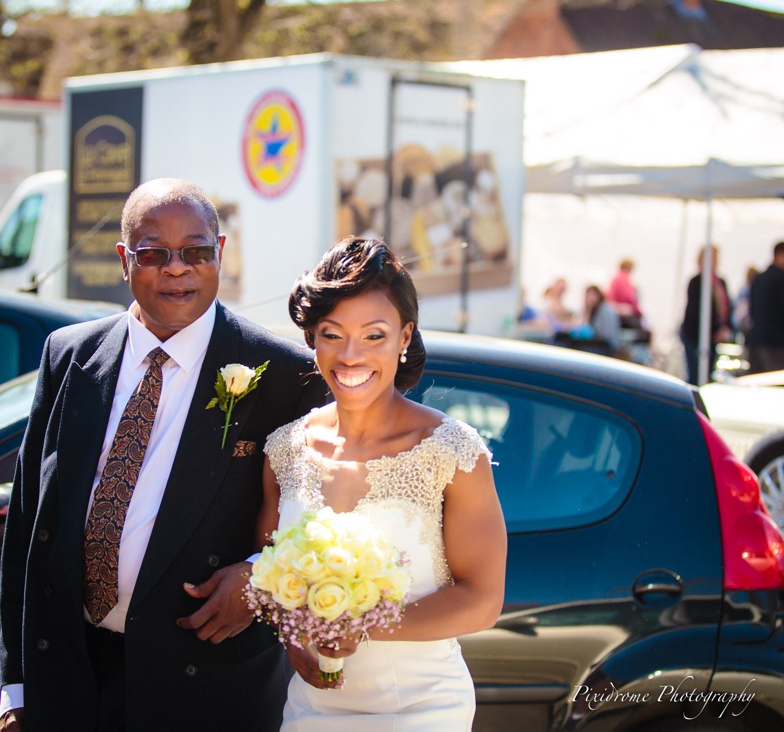 The bride arriving on her father's arm, spring market stalls behind