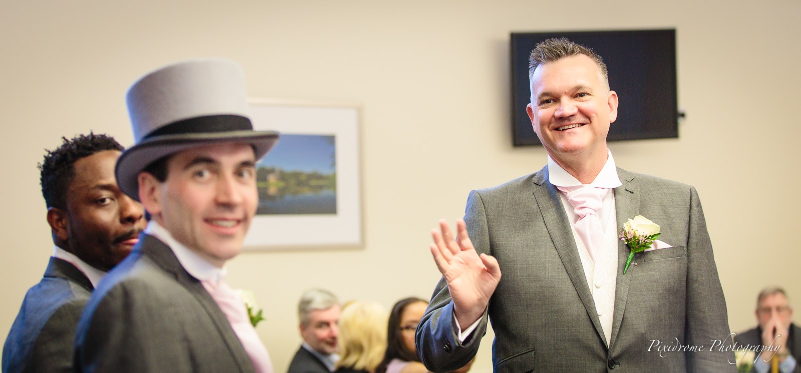 The groom waving beside a groomsman in a grey top hat before the ceremony