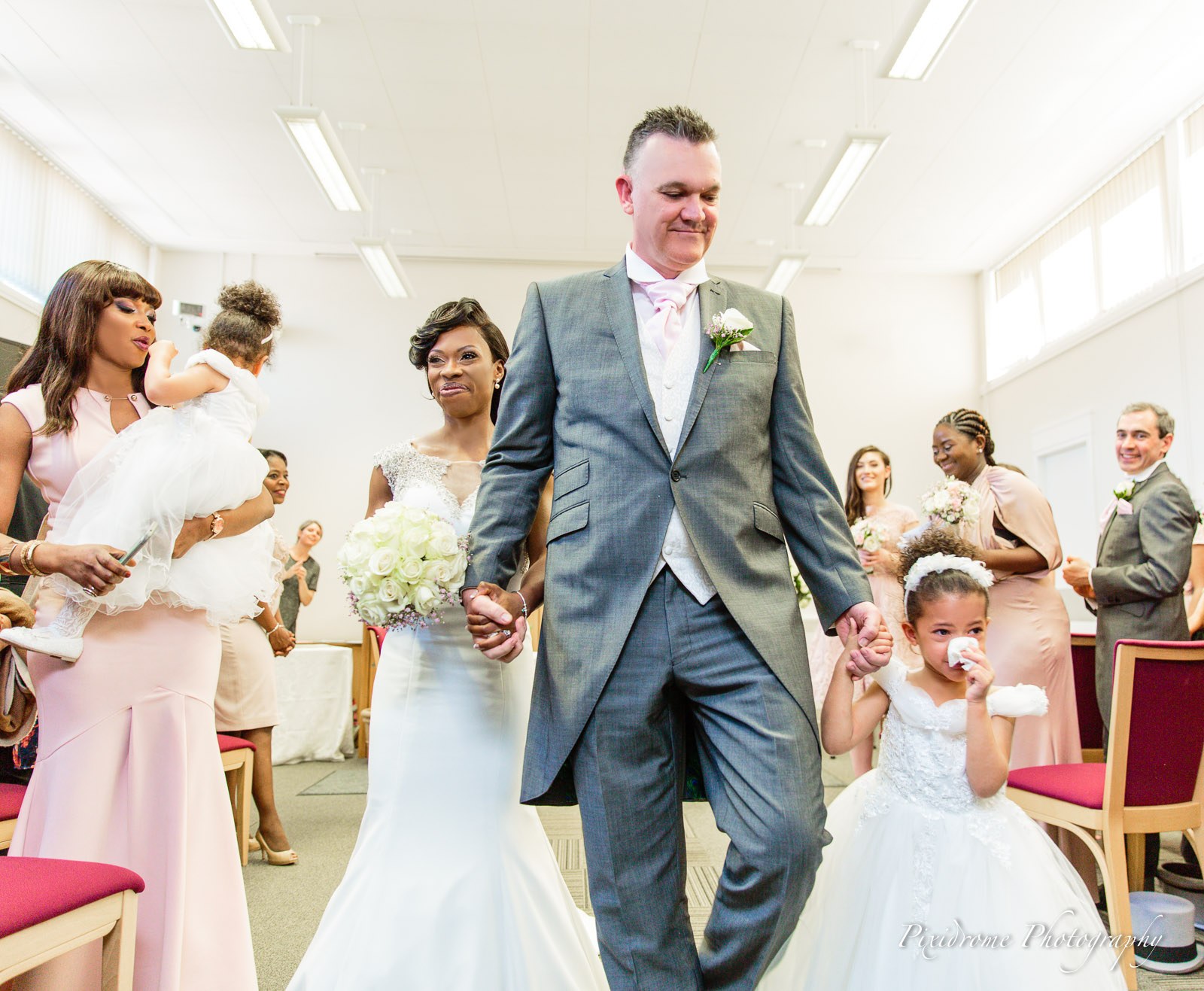 The newlyweds walking back down the aisle, a flower girl at their side