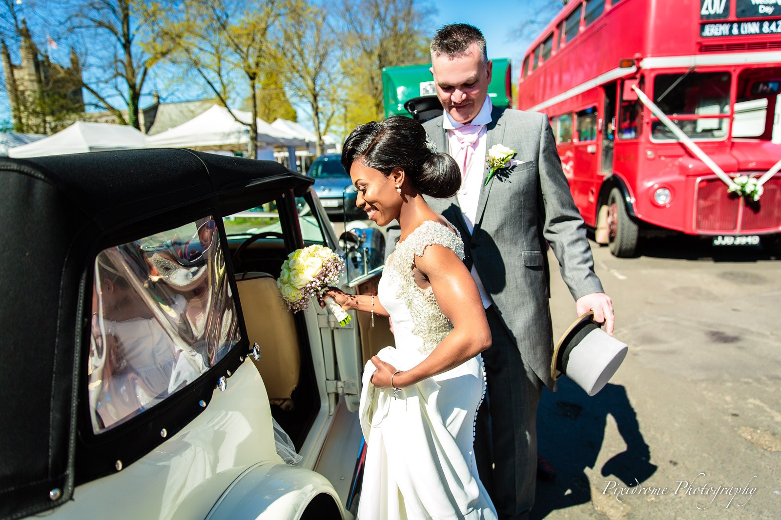 The couple by their vintage car with a red Routemaster bus behind