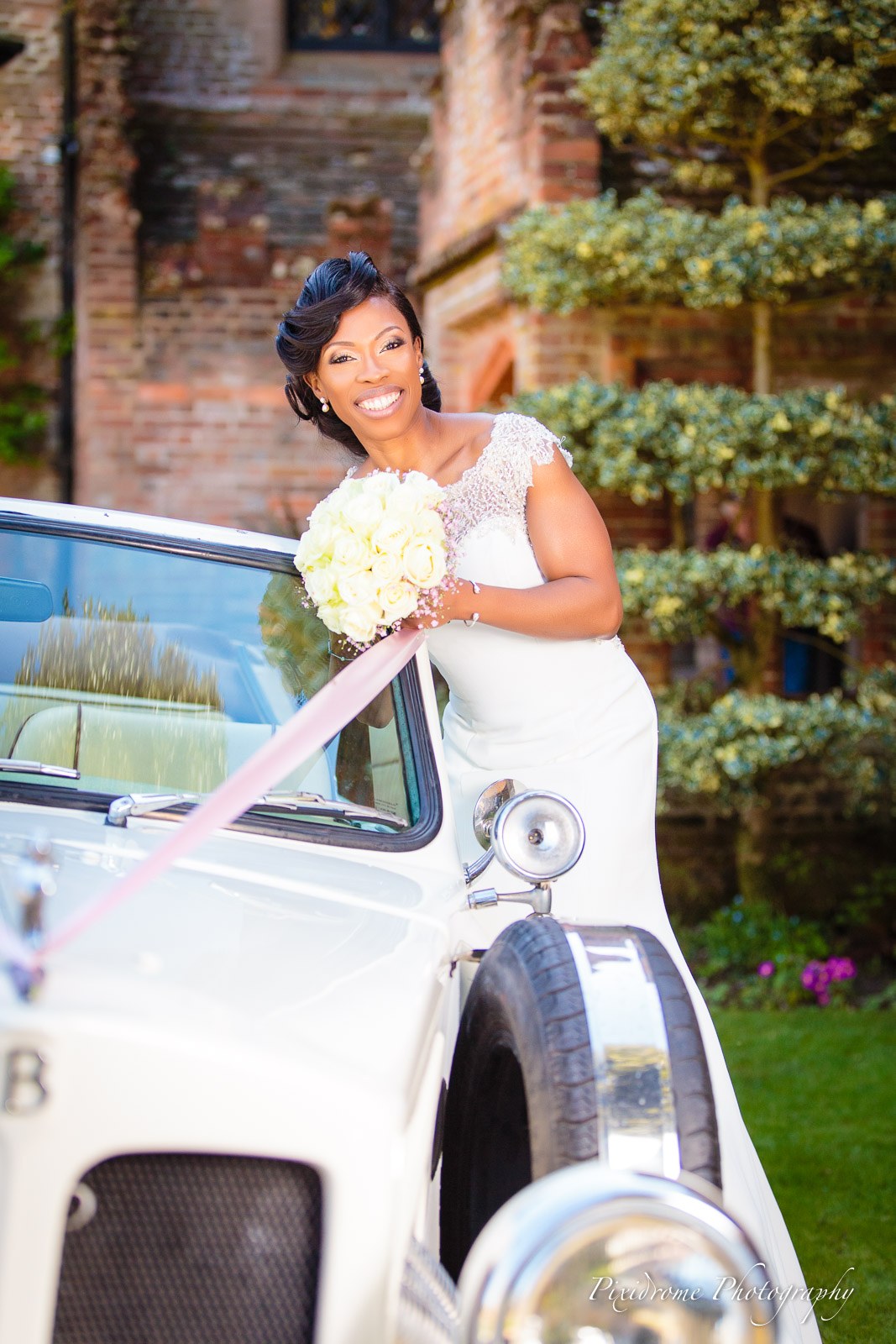 The bride leaning on the ribboned vintage car in the grounds of Chenies Manor House