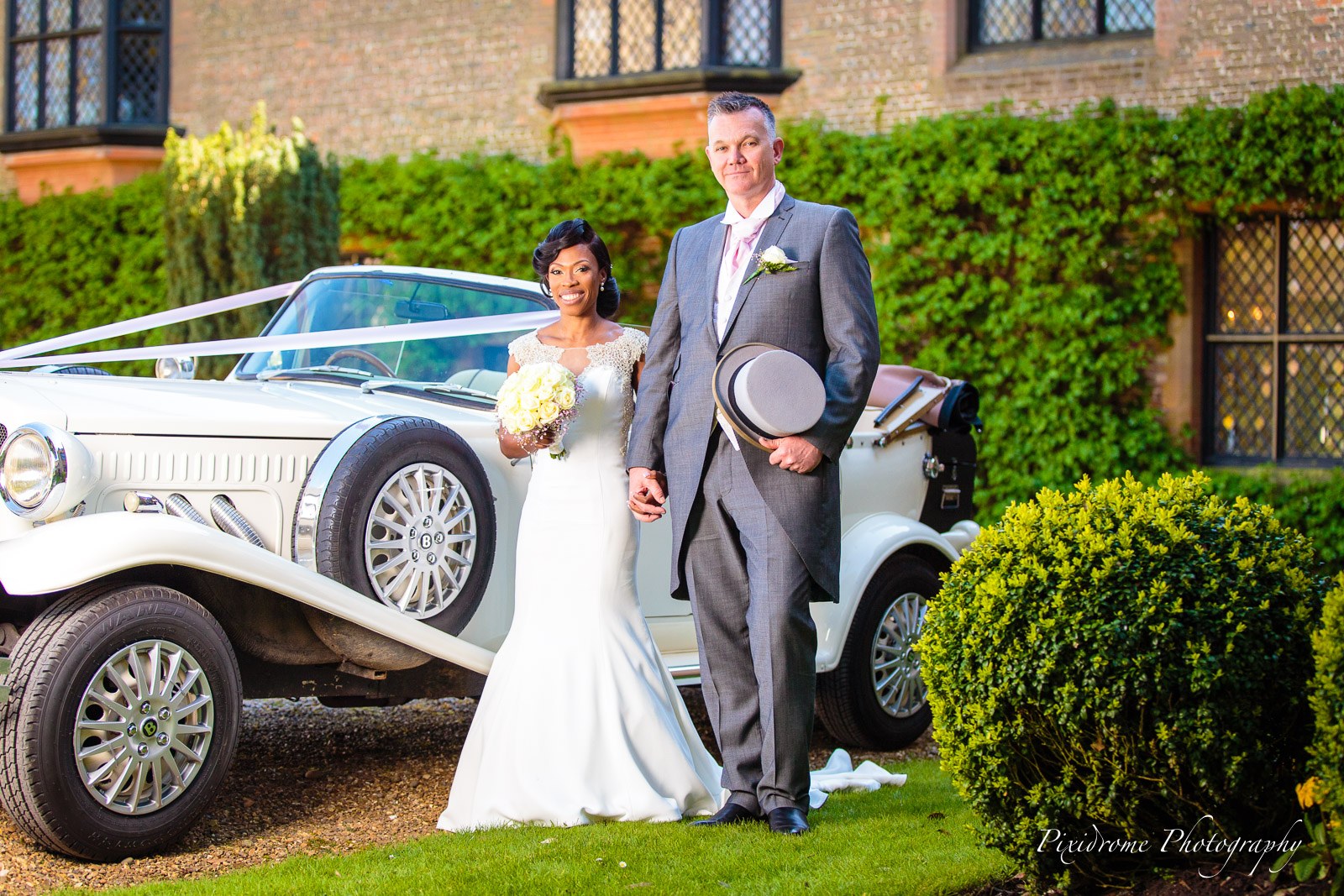 The couple by the vintage white car before the brick frontage of Chenies Manor House