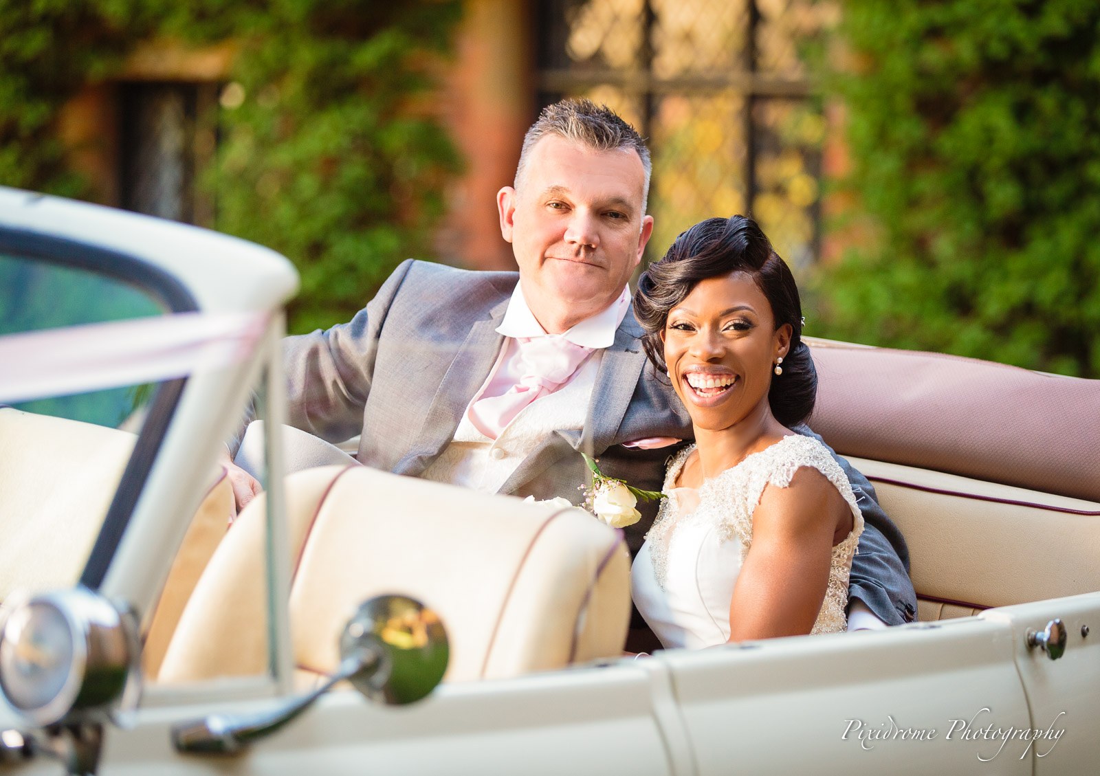 Bride and groom seated in the open-topped vintage wedding car