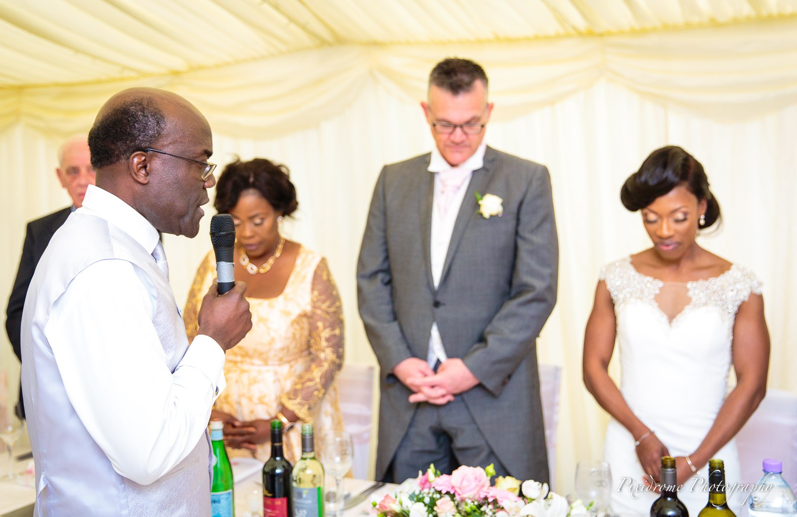 A guest leading a blessing at the top table as the couple bow their heads