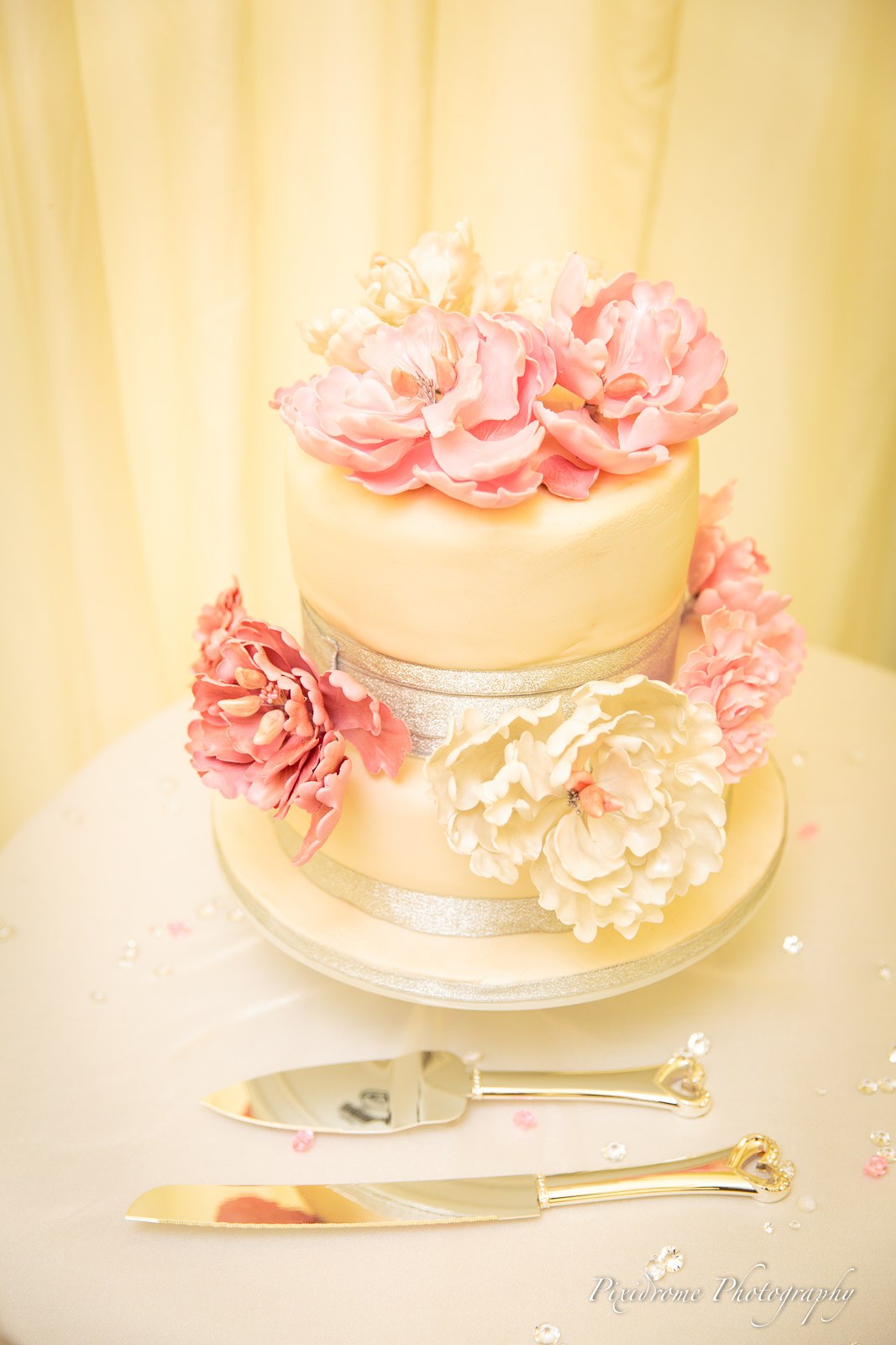 The two-tier ivory cake dressed with pink sugar peonies and a cake knife