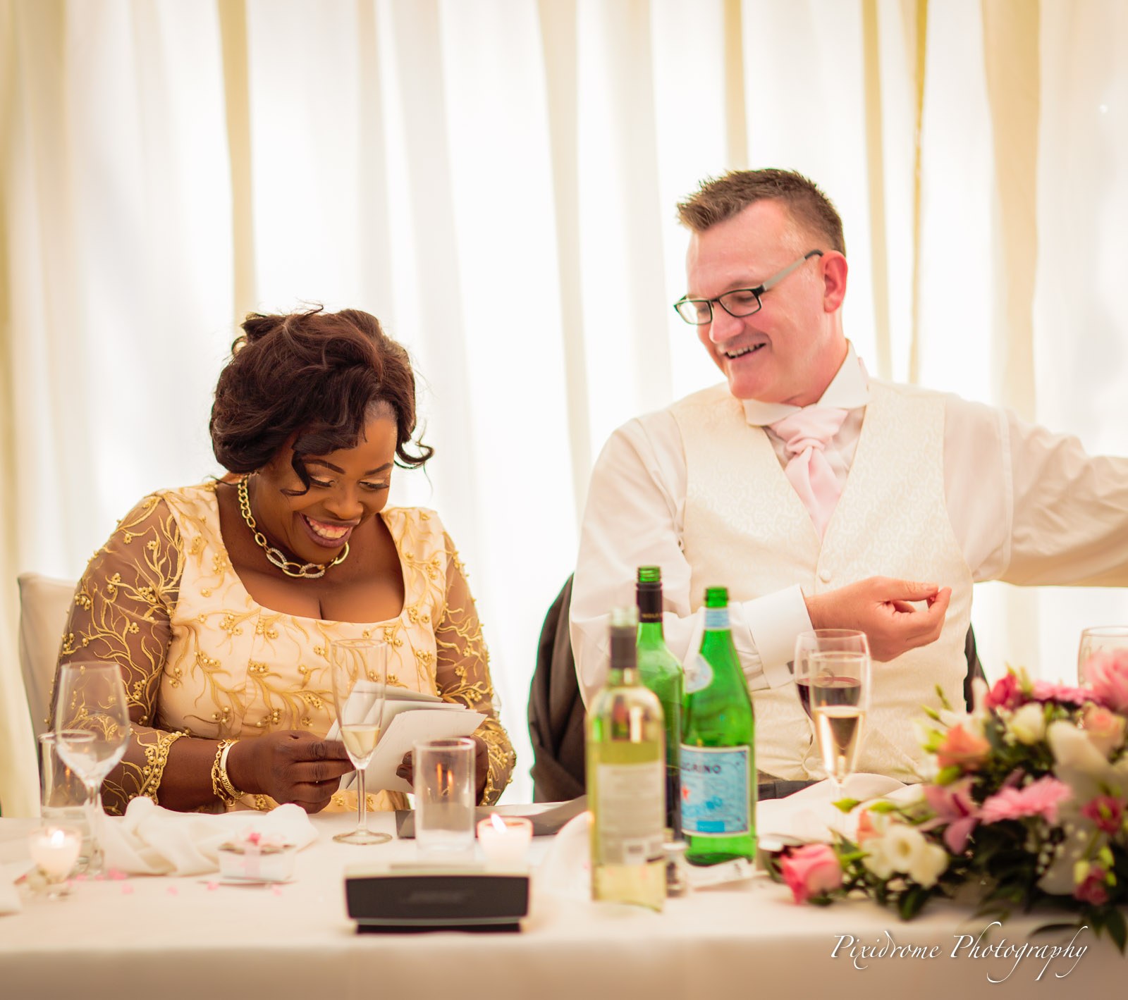The groom laughing as the mother of the bride reads a card at the top table