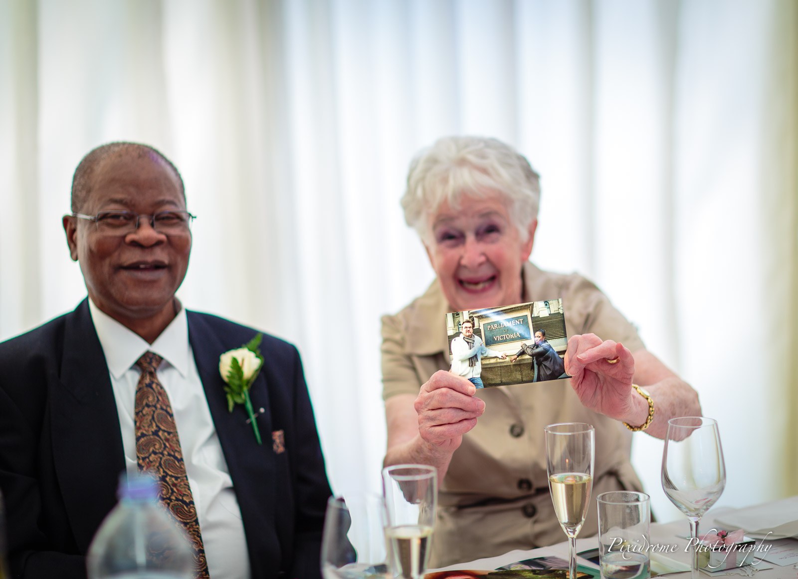 The father of the bride and a guest holding up a photograph and laughing