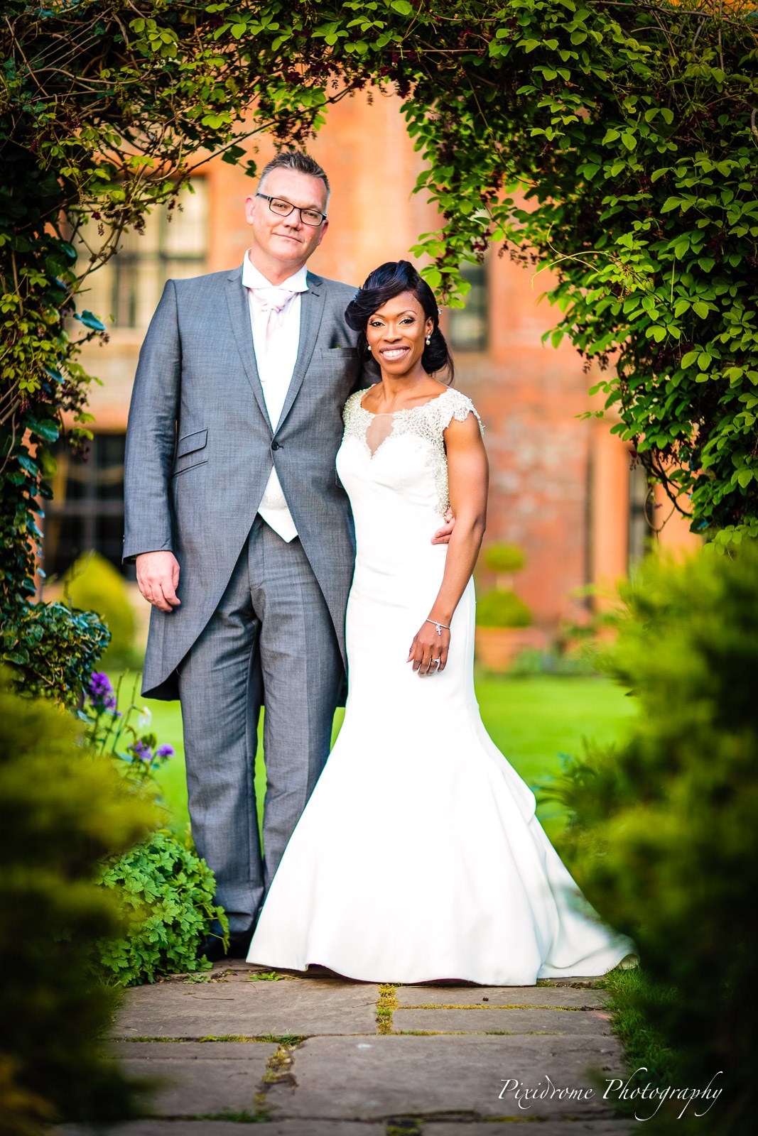The couple beneath a leafy arch before the brick facade of Chenies Manor House