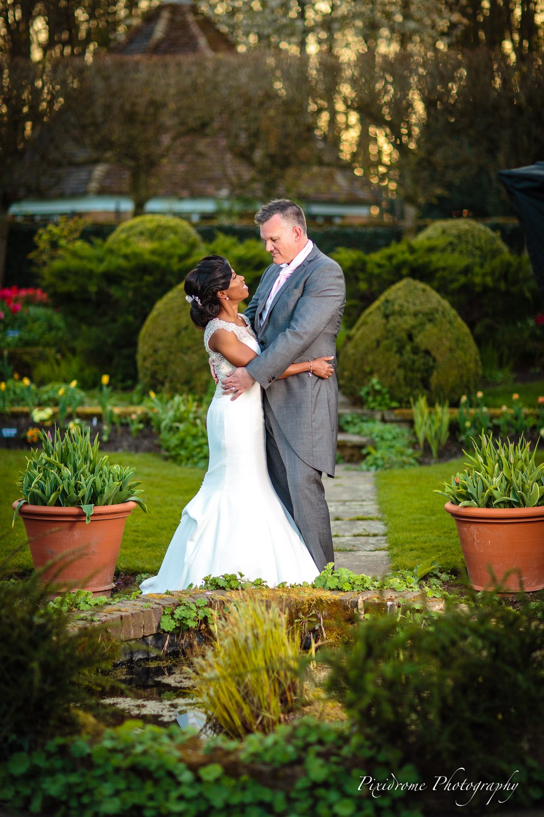 Bride and groom embracing in the topiary gardens of Chenies Manor House