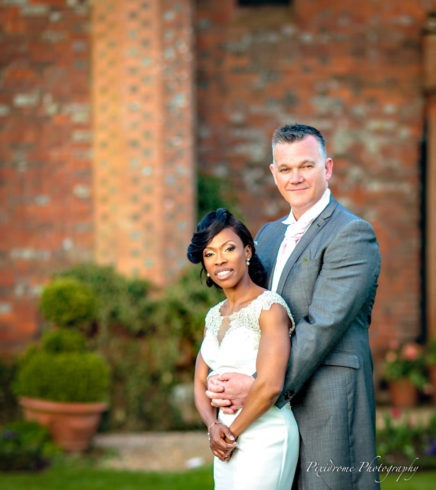 The couple embracing by a brick wall in the gardens of Chenies Manor House