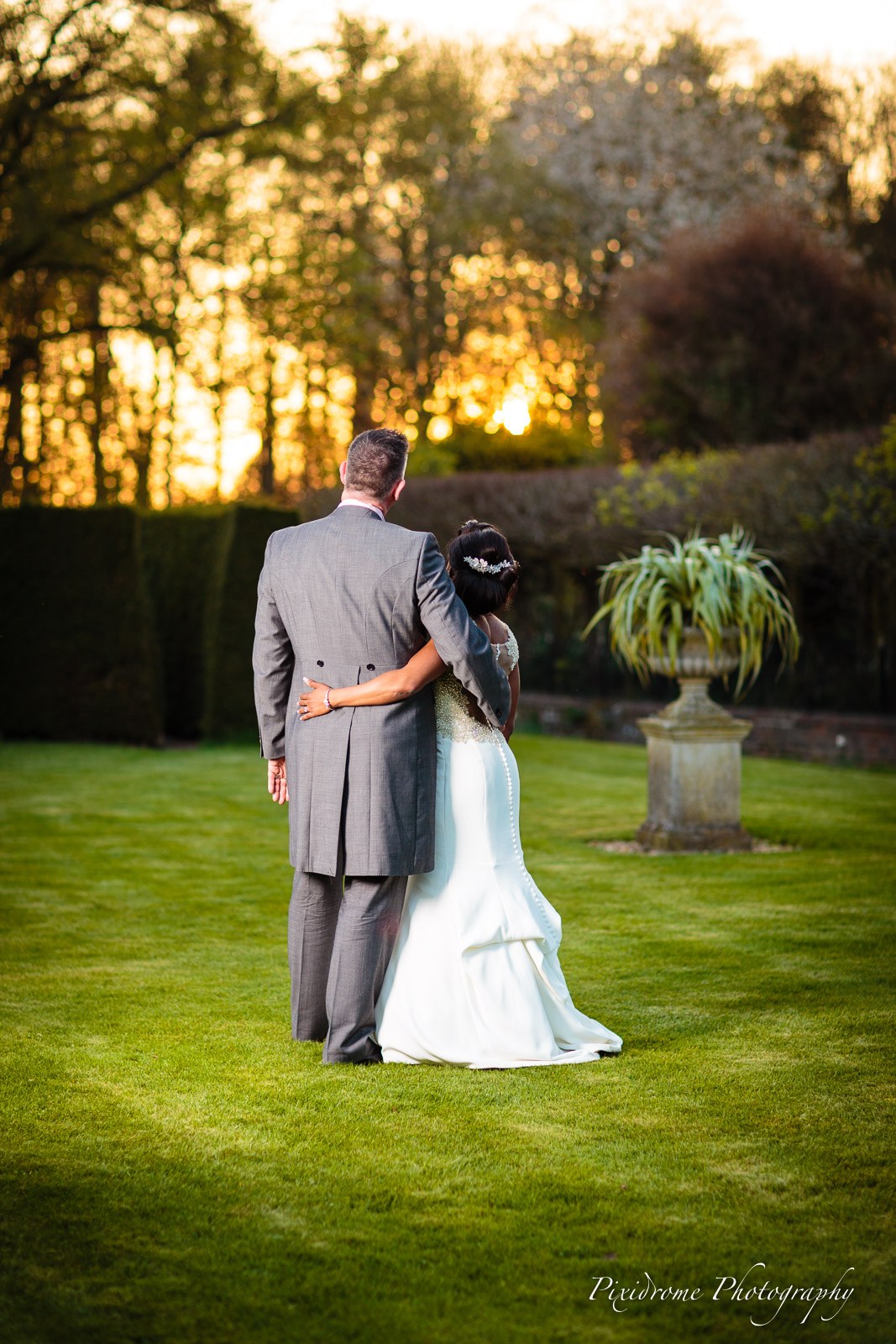 The couple looking over the lawn at Chenies Manor House at sunset beside a stone urn