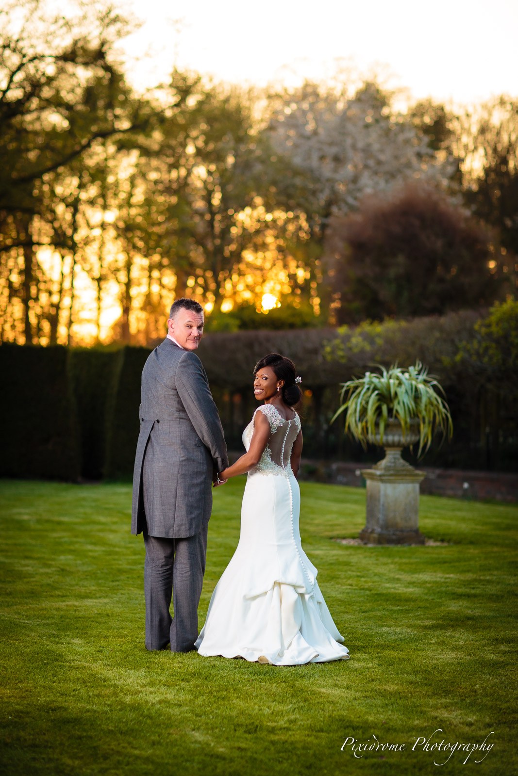 Bride and groom holding hands on the lawn at Chenies Manor House at sunset