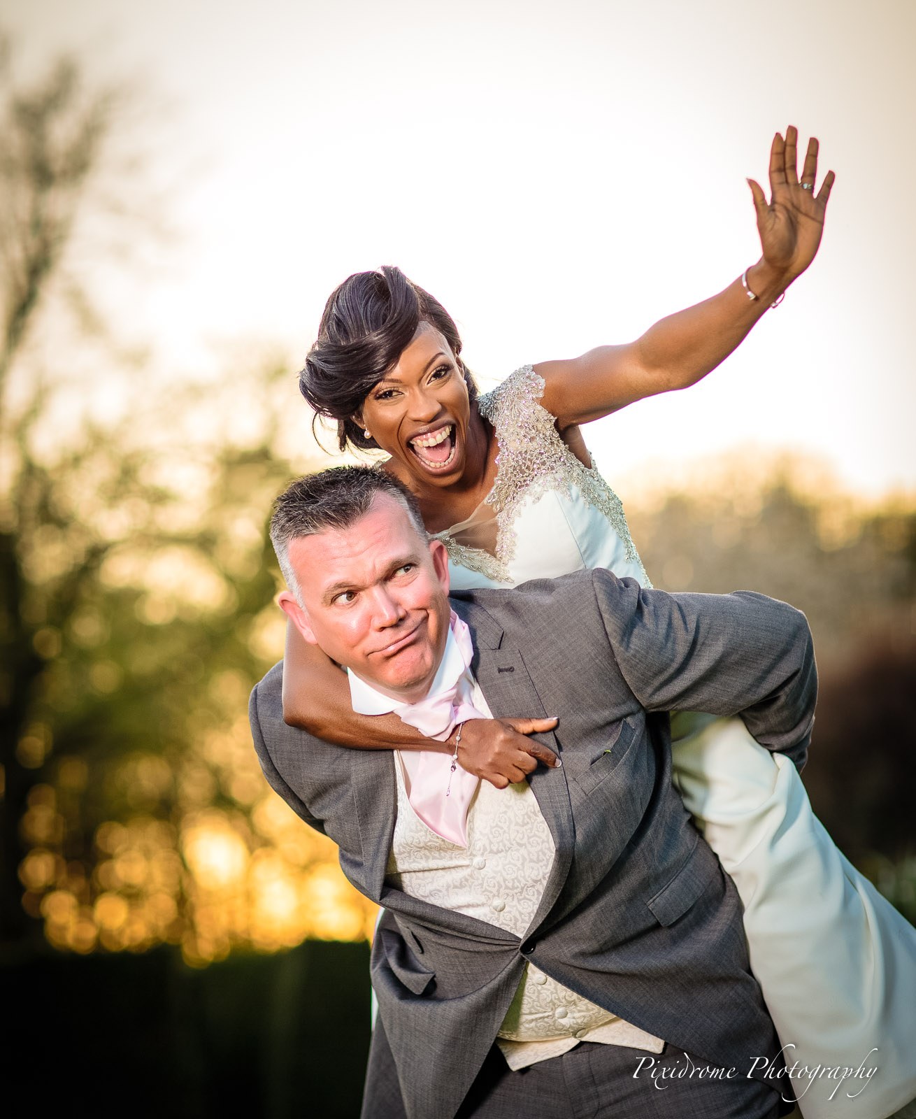The bride riding on the groom's back against the sunset at Chenies Manor House