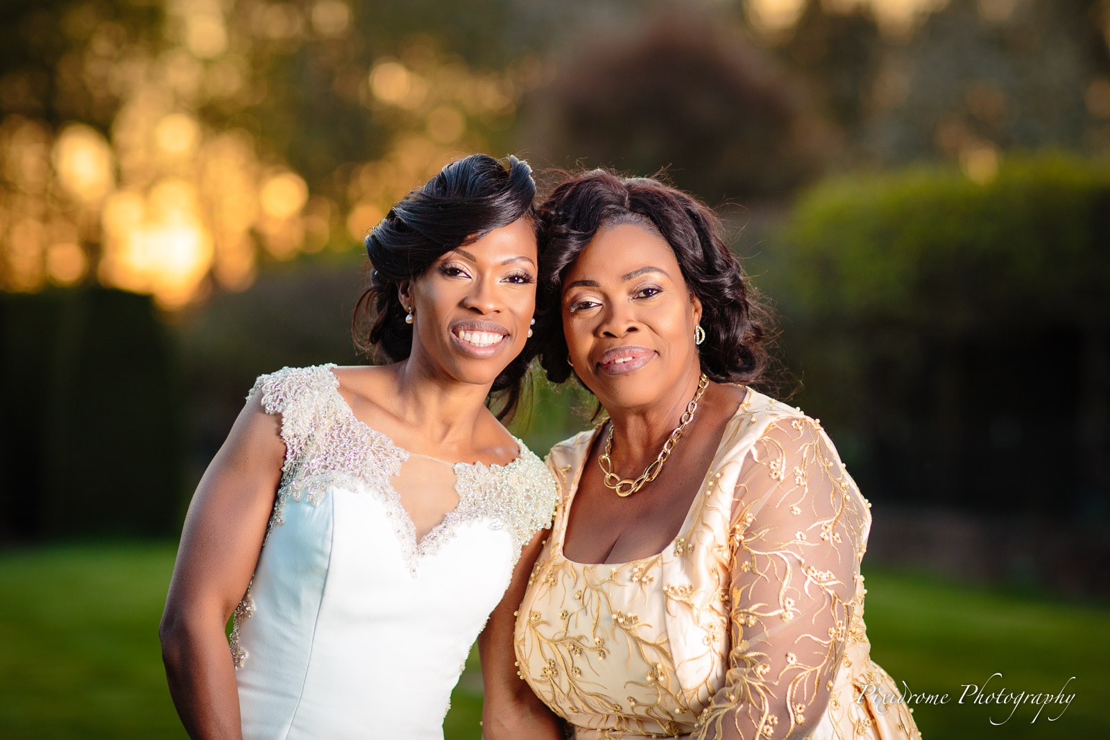 The bride cheek to cheek with her mother in golden evening light