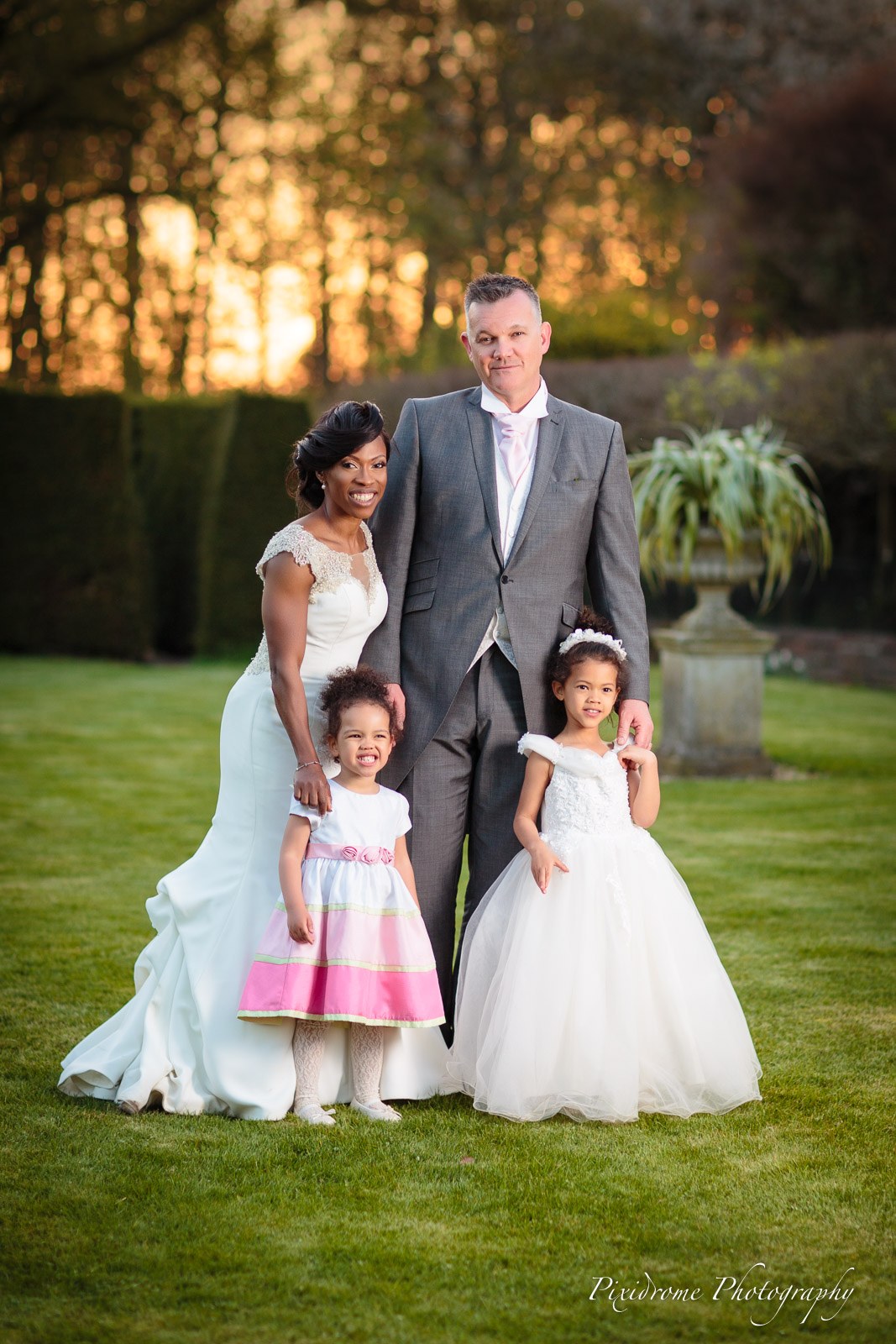 The couple with two flower girls on the lawn at Chenies Manor House at sunset