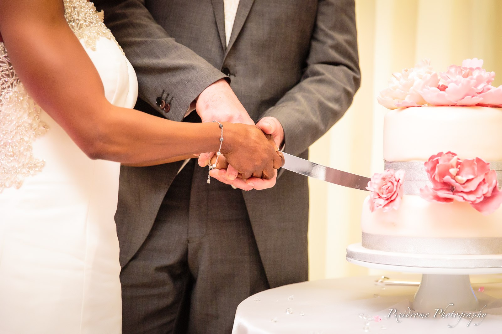 Close-up of the couple's hands cutting the pink-peony cake