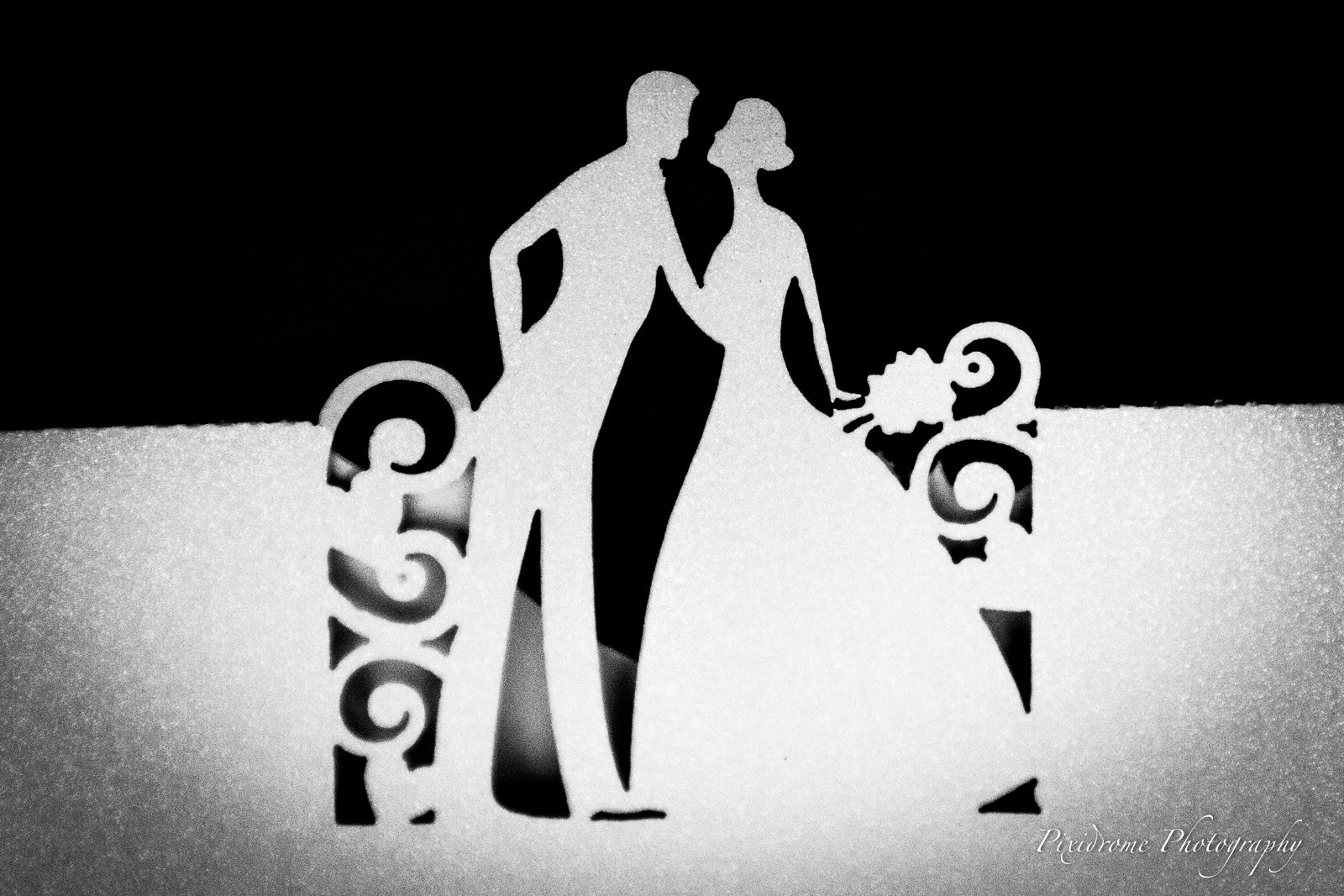 Black-and-white silhouette cake topper of a couple standing beside an ornate bench