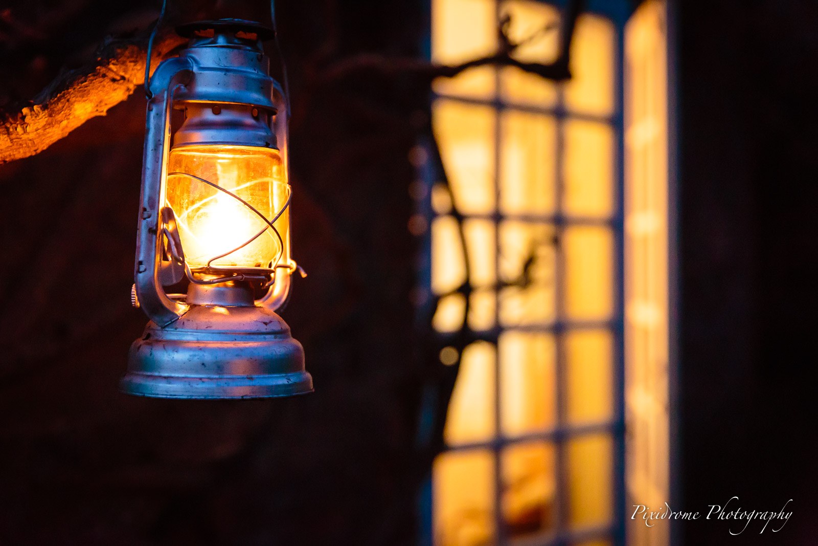 A lit hurricane lantern hanging by a leaded window at dusk