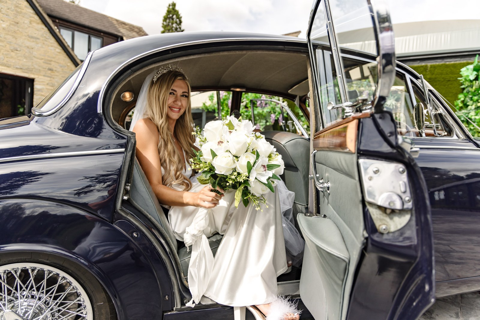 The bride arriving in a navy vintage car, her white bouquet in her lap