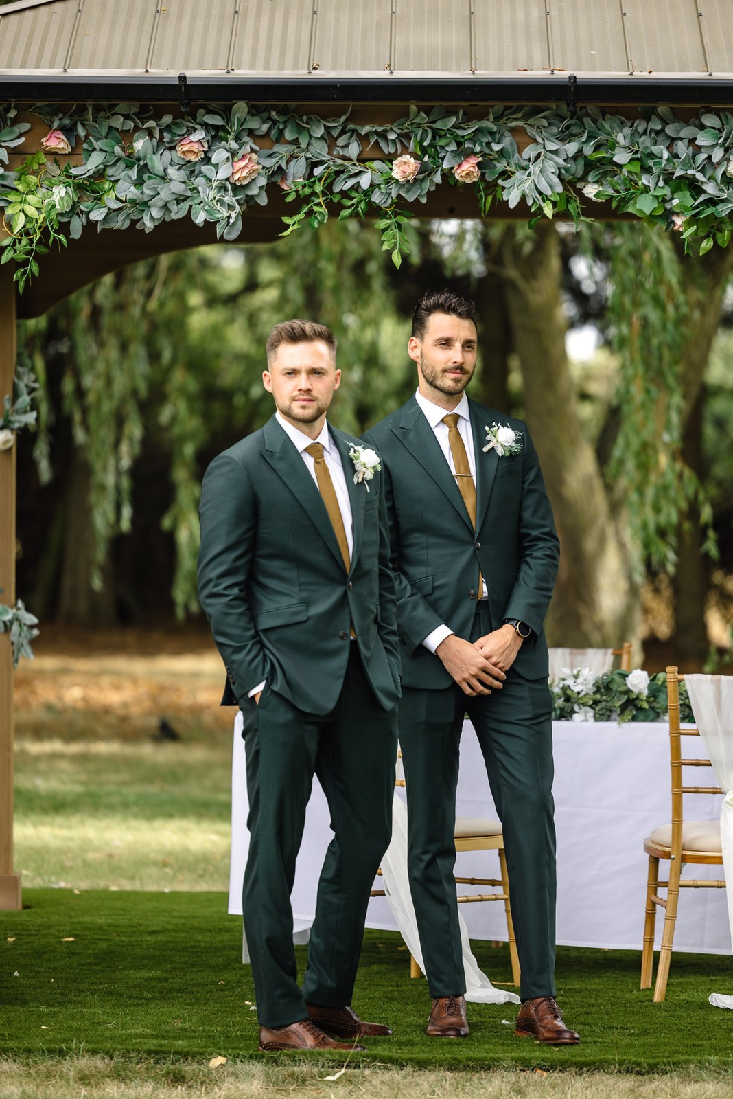 The groom and best man in green suits waiting beneath the foliage ceremony arch