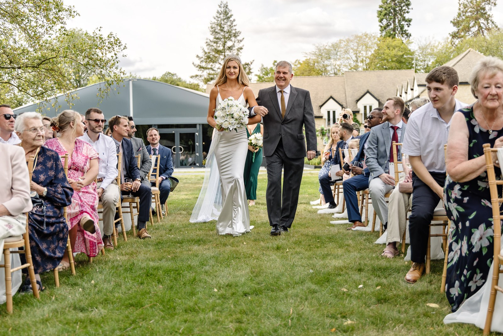 The bride walking the outdoor aisle on her father's arm as guests look on