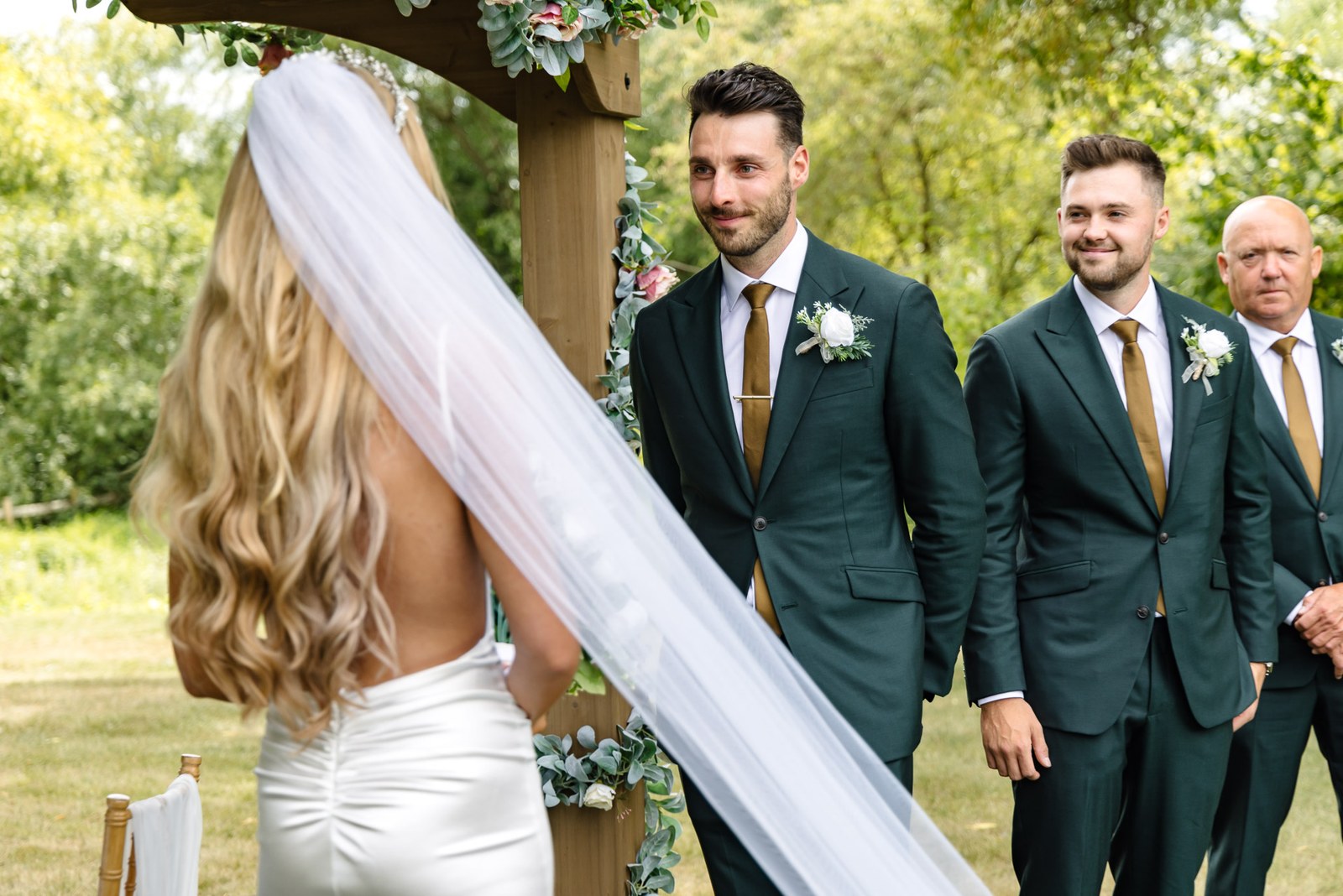The bride facing the groom and groomsmen, her long veil trailing behind