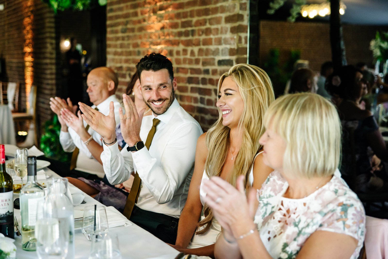 Guests clapping at the top table during the speeches, exposed brick behind