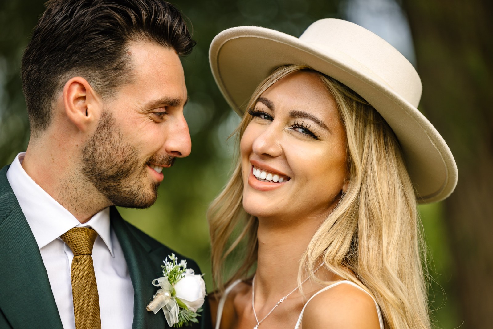 A close portrait of the couple, the bride in her fedora, the groom smiling