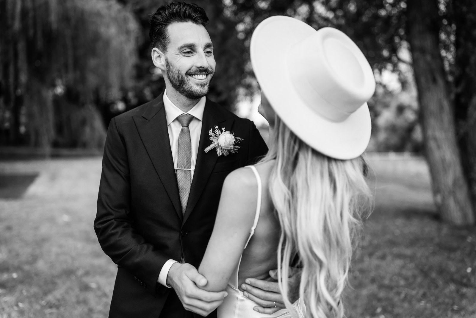 Black-and-white of the laughing groom with the bride on a wooded path