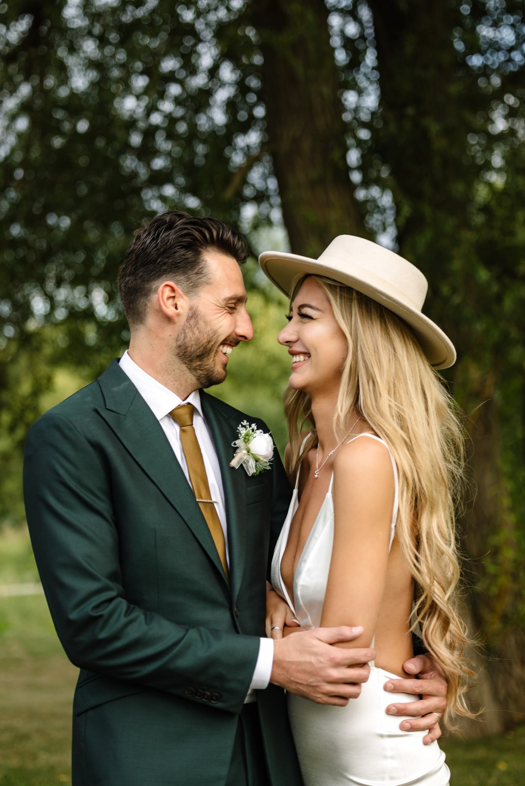 The couple embracing beneath a tree, the bride in a fedora