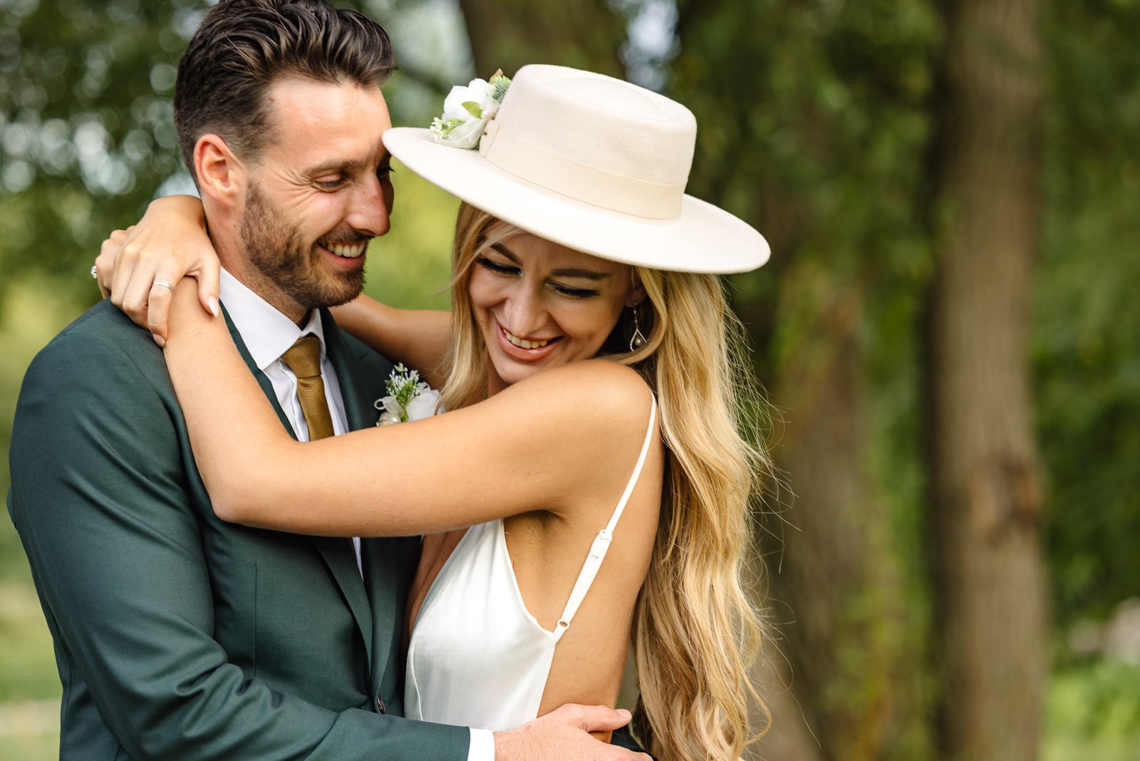 The couple laughing in a close embrace, the bride's fedora tilted