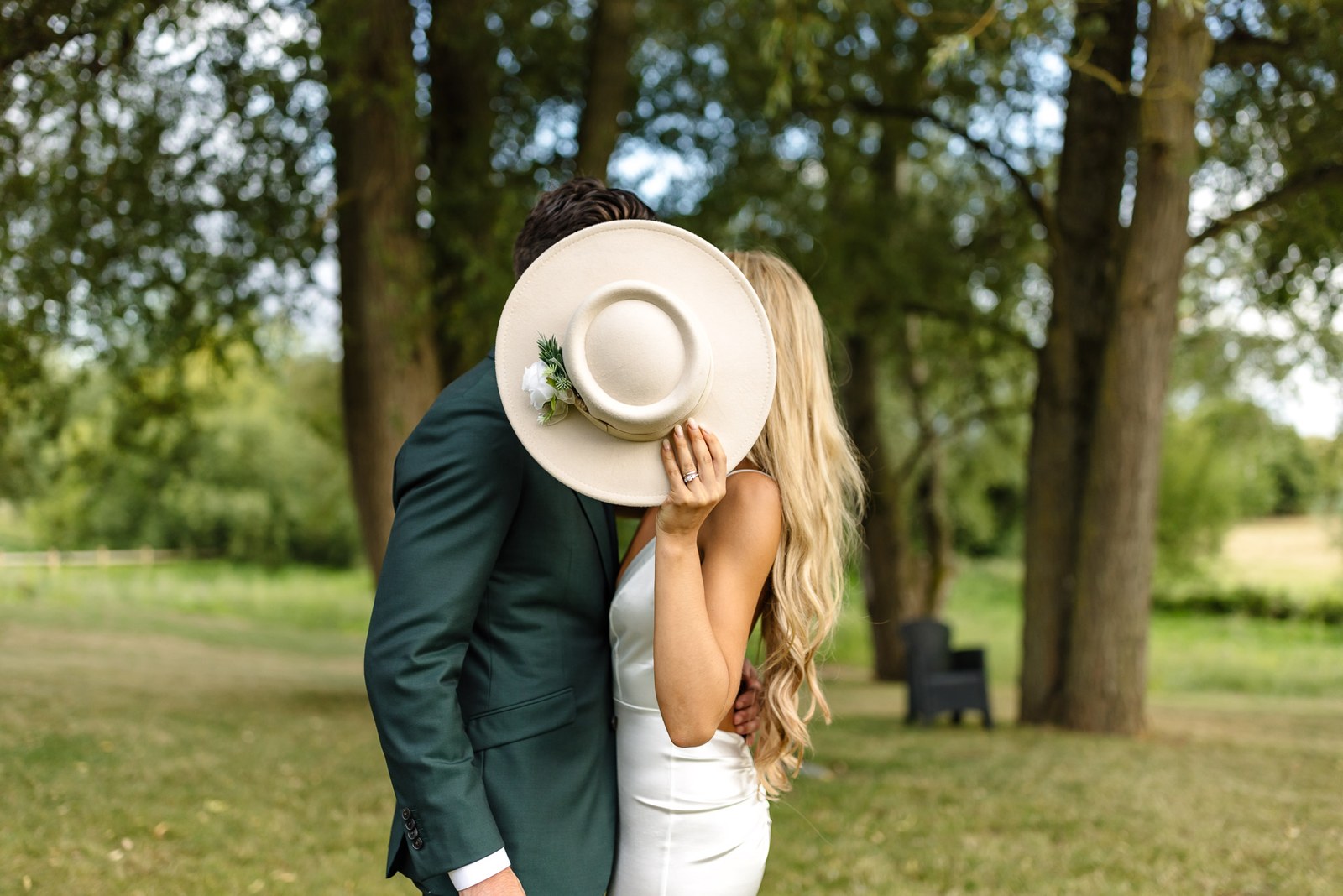 The couple embracing as the bride hides her face behind her hat