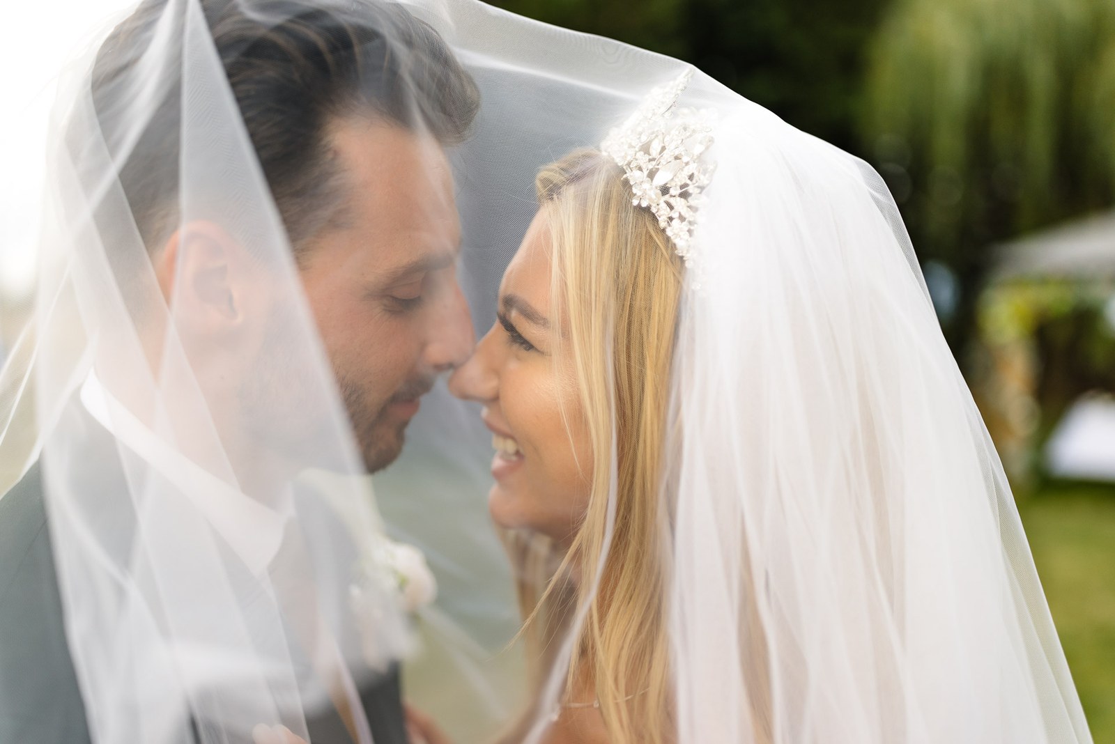 The couple under the veil, noses touching, in a tender portrait