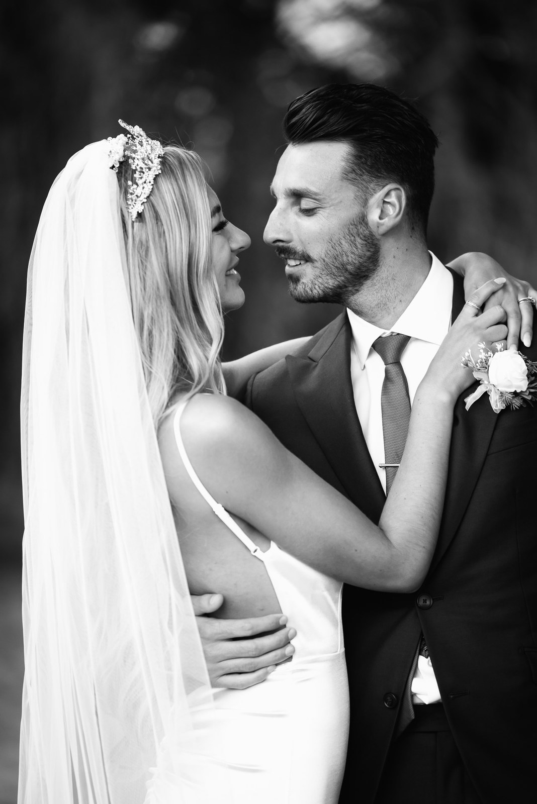 Black-and-white of the couple embracing, the groom gazing at the bride