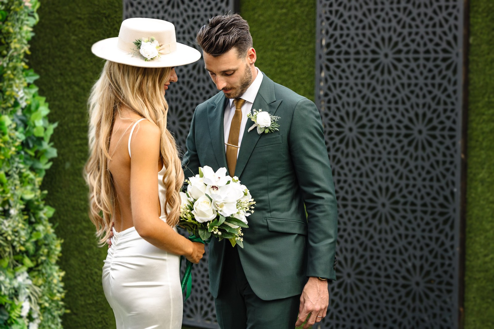 The couple by a green foliage wall, the groom looking at the bride