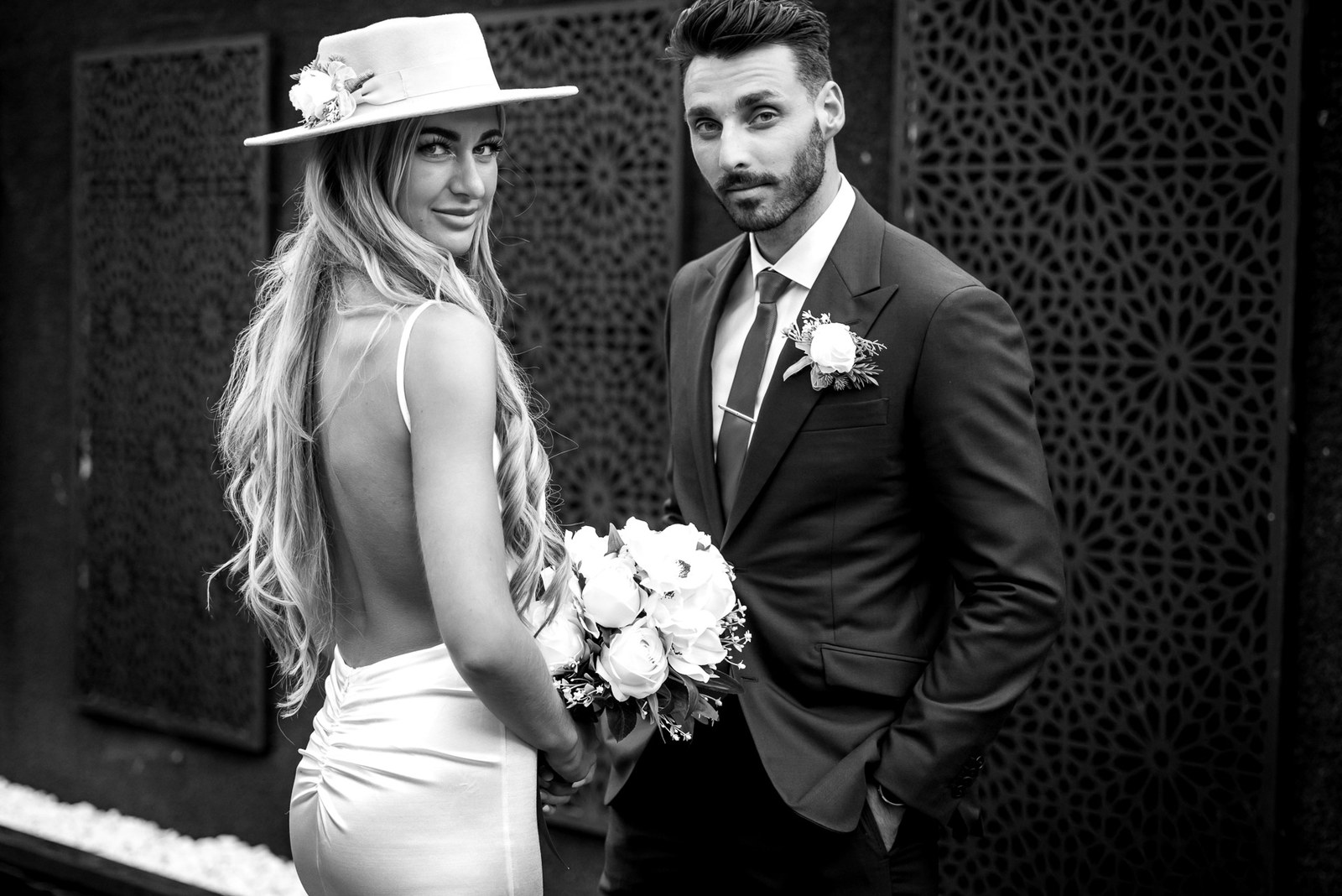 Black-and-white of the couple by a patterned dark wall, the bride glancing back