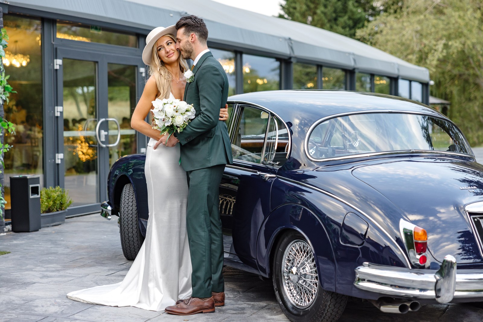 The couple by the vintage car outside the glass garden room of the Chesterton Hotel