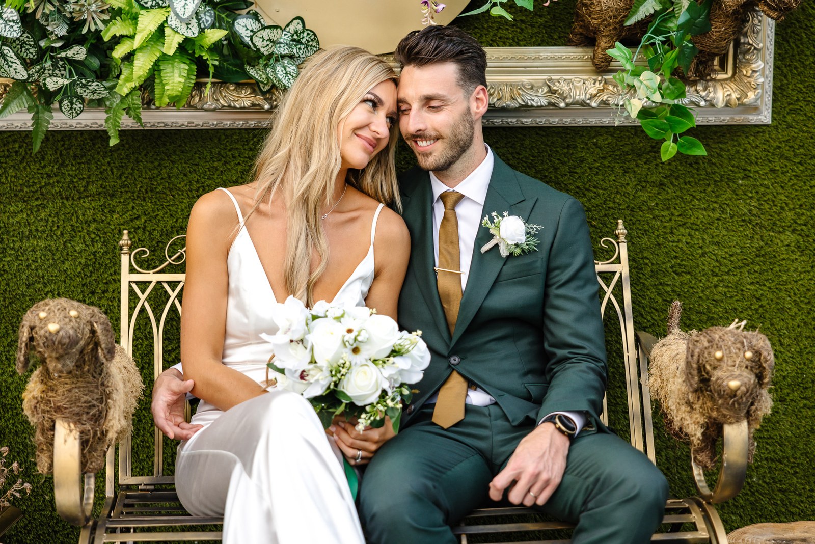 The couple seated on an ornate bench by a foliage wall at the Chesterton Hotel