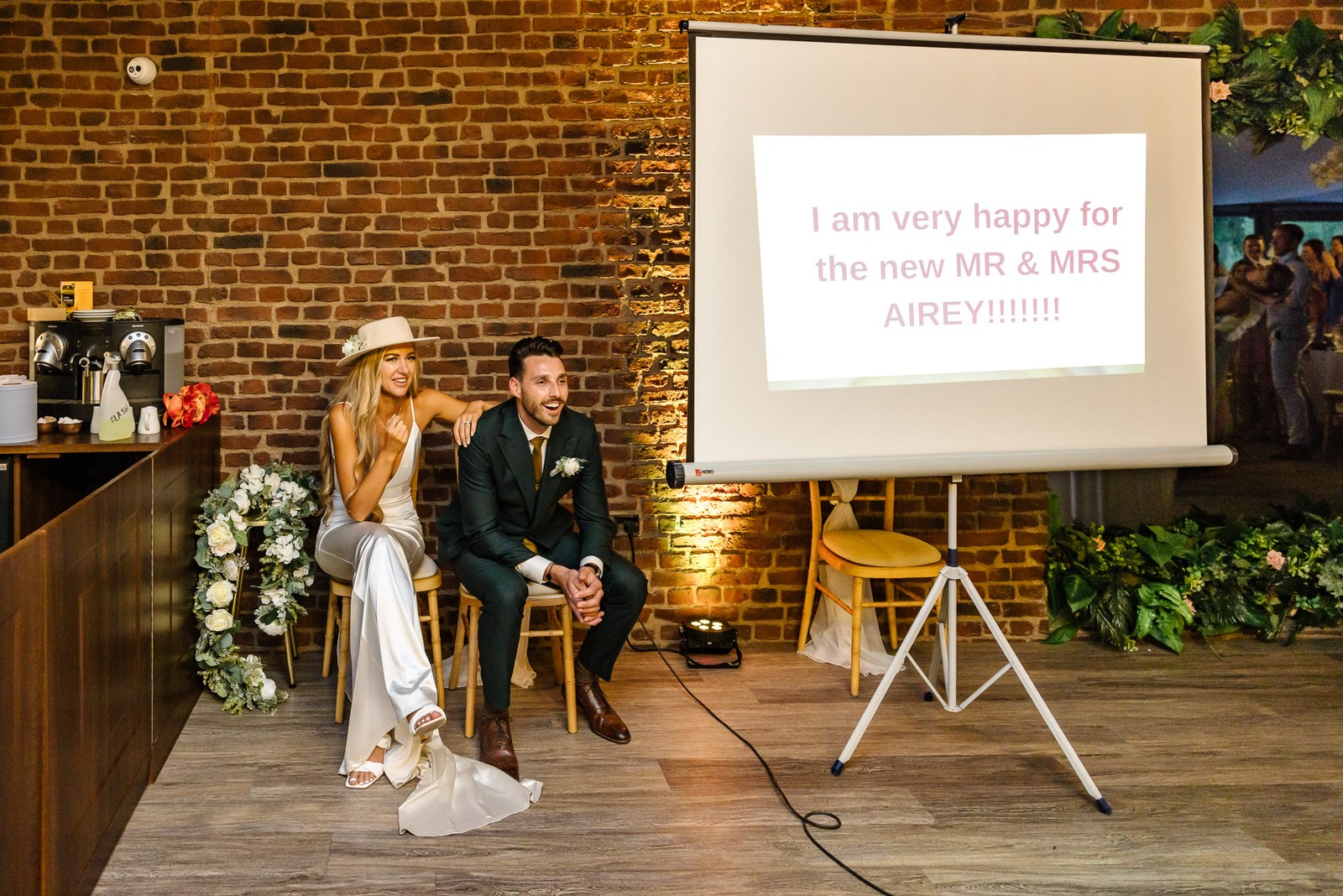 The couple seated at the bar beside a projected congratulations message