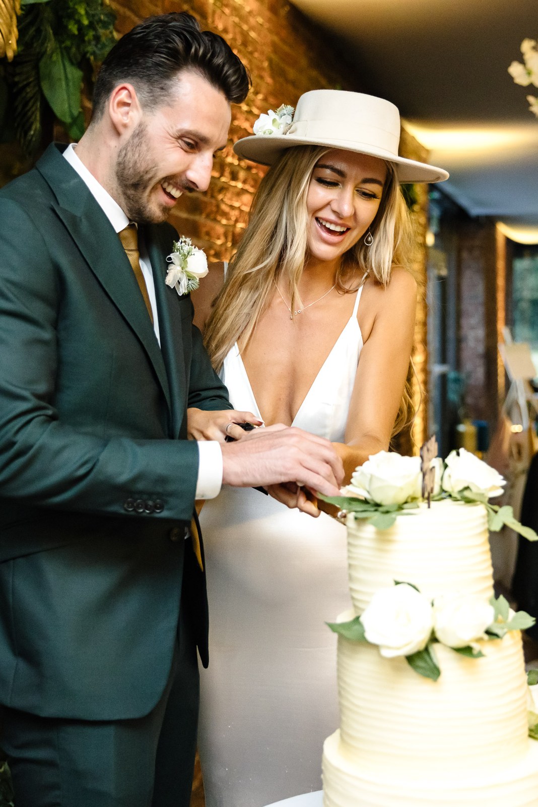 The couple cutting their cake together, the bride in her fedora
