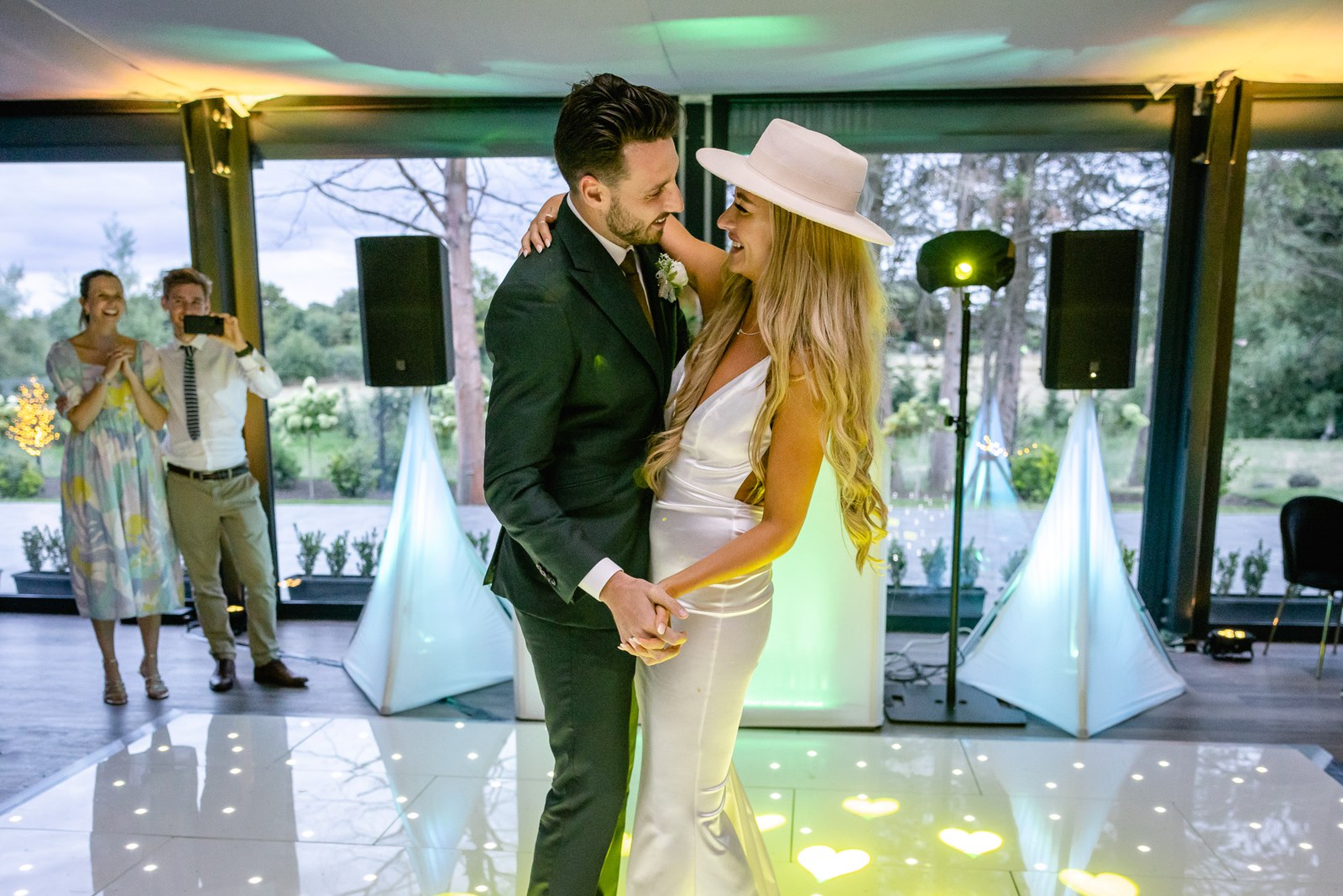 The couple dancing close under coloured lights by the glass wall