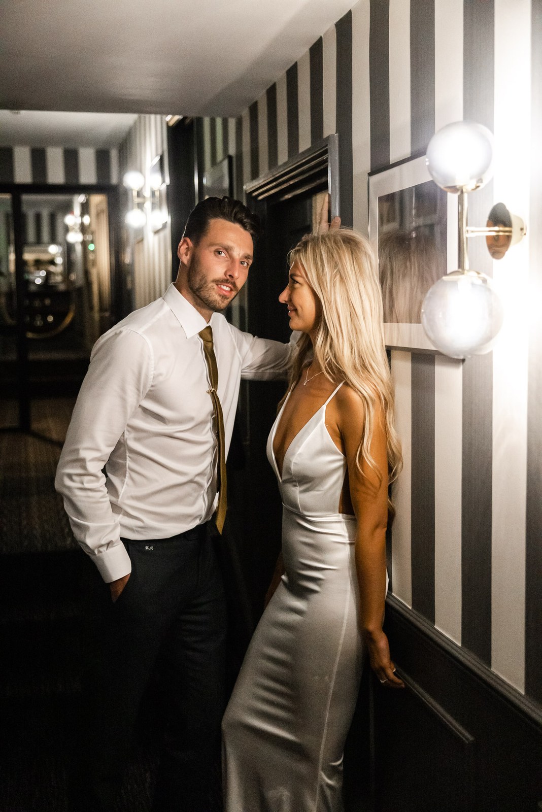 The couple in a striped hotel corridor, the bride gazing at the groom