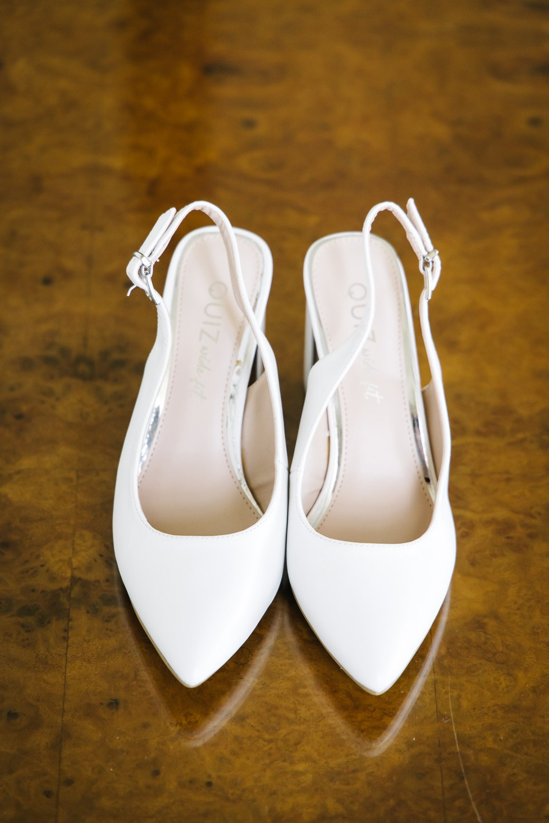 Close-up of the bride's white pointed slingback shoes on a polished wood surface
