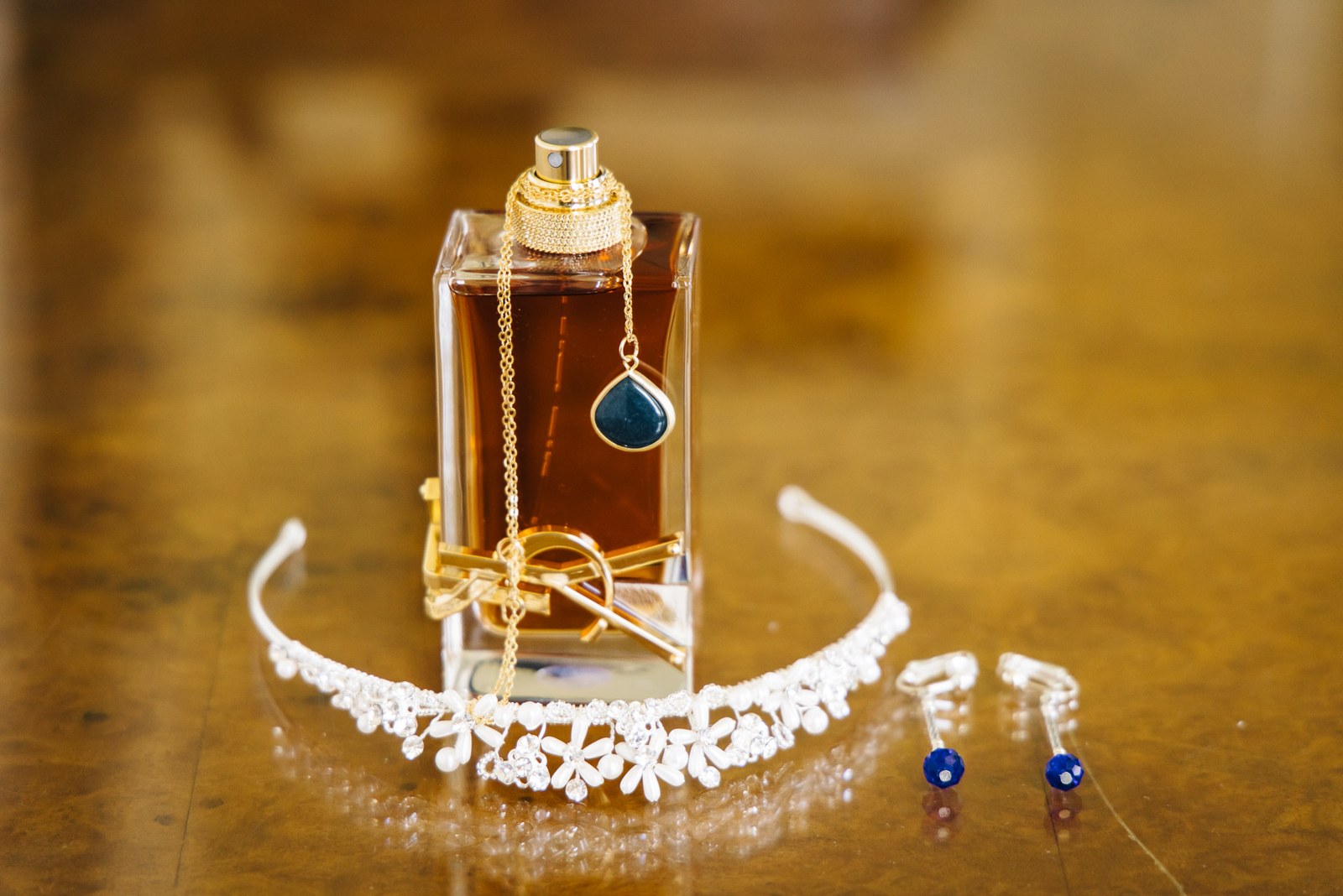 Perfume bottle, tiara and earrings arranged together on a polished wooden table
