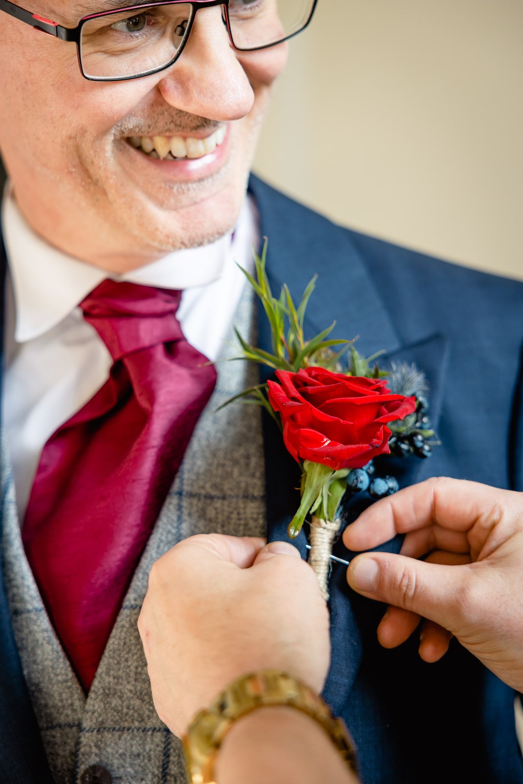 A red rose buttonhole being pinned to the lapel of a navy suit