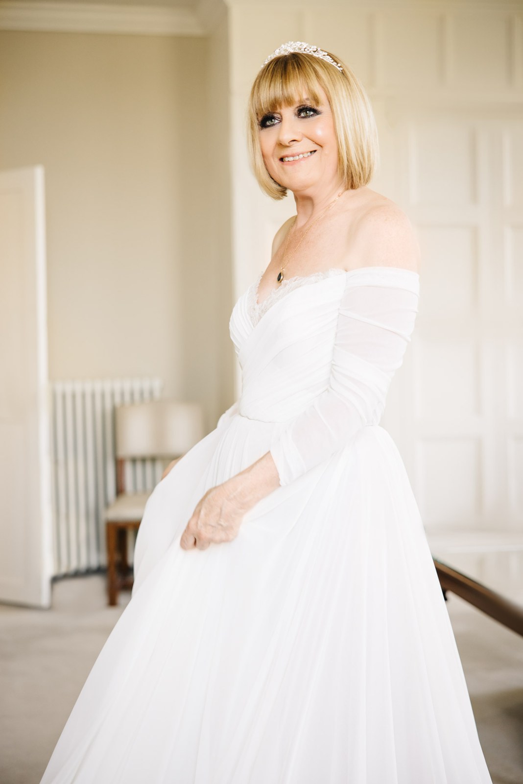 Bride in an off-shoulder tulle gown and tiara, smiling in full length