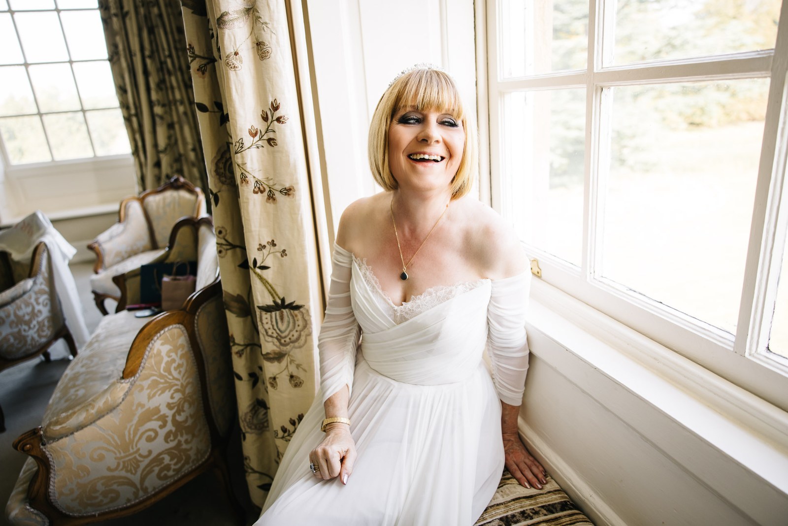Bride laughing by a bright window in her off-shoulder gown